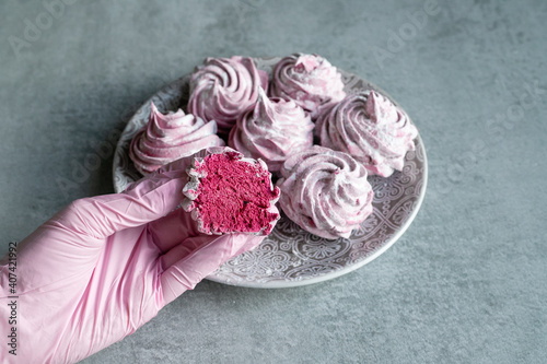 A pink-gloved hand holds a pink marshmallow with marshmallows in the background. Delicious sweets, dessert, healthy sweets