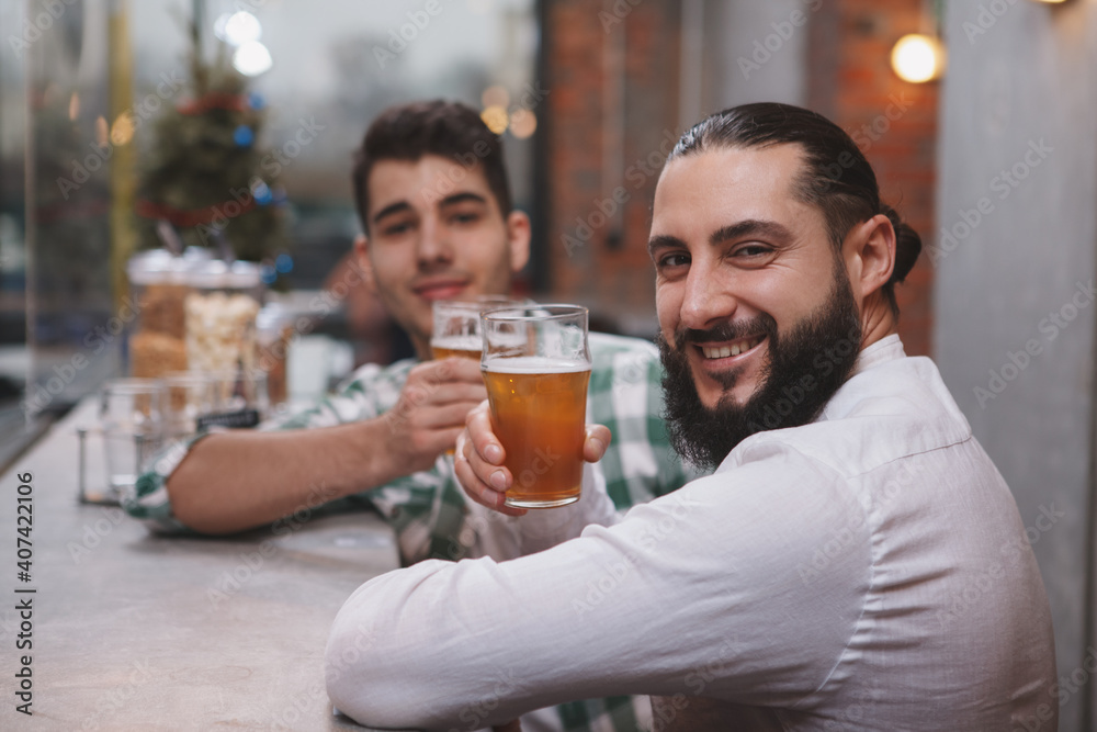 Happy bearded man smiling to the camera, holding up his beer glass at the pub