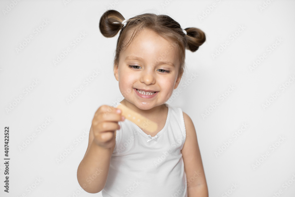 Wound, cut, medicine and healthcare concept. Close up studio shot of happy smiling little kid girl, holding in hands adhesive plaster bandage and looking at it. Focus on baby's face Wound, cut, medicine and healthcare concept. Close up studio shot of happy smiling little kid girl, holding in hands adhesive plaster bandage and looking at it. Focus on baby's face