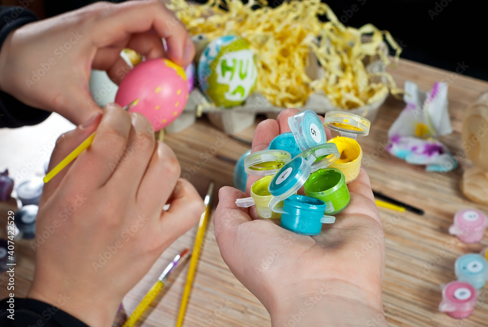 Mother and son paint Easter eggs. Multicolored Easter eggs on a wooden table background. Traditional family entertainment before the holiday.