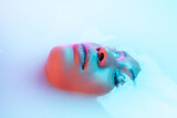 Delighted. Beautiful female face in the milk bath with soft glowing in blue-pink neon light. Copyspace for advertising. Modern neoned colors, foam. Beauty, fashion, style, skincare concept. Attractive