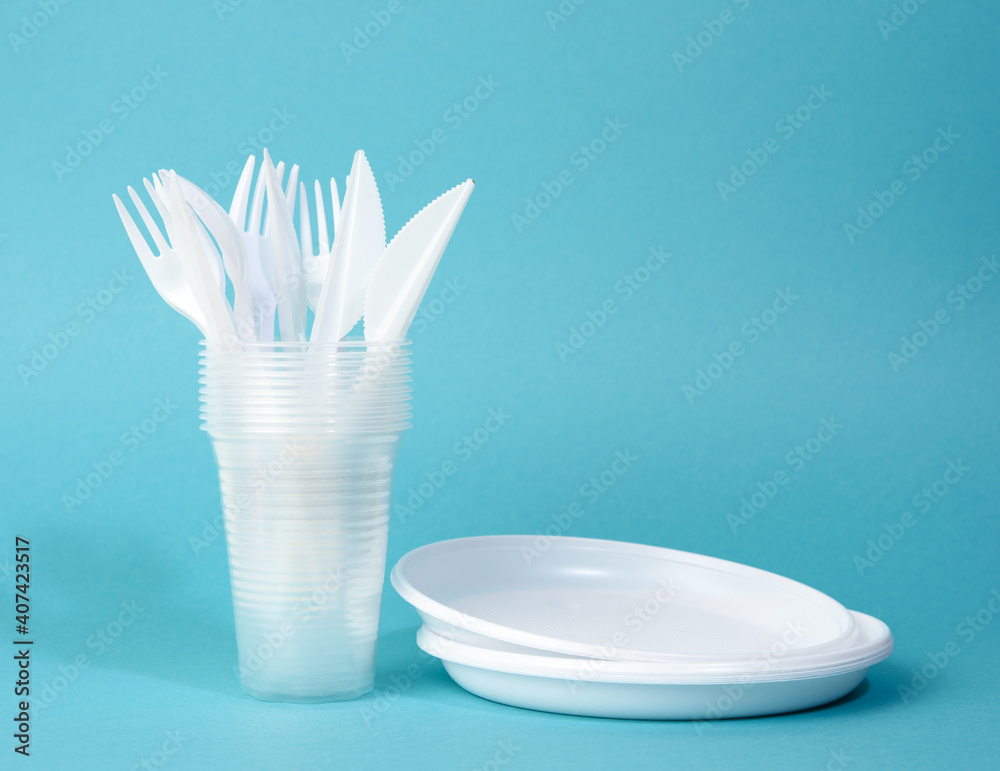 disposable white plastic tableware plates, cups, forks and knives on a blue background disposable white plastic tableware plates, cups, forks and knives on a blue background