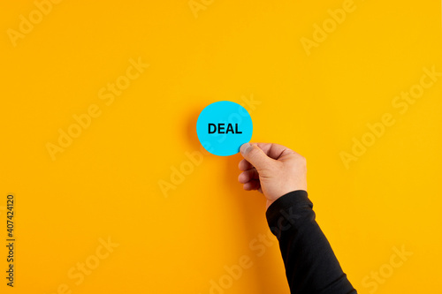 Male hand placing a blue badge with the word deal on yellow background. Business deal or agreement