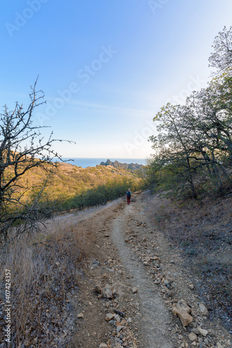 a female tourist walks along a mountain trail, at sunset, a panorama of a mountain range on the horizon .vertical photo