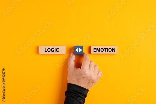 Male hand holds a wooden cube with arrow icon between the options of logic or emotion. Emotional or logical decision making