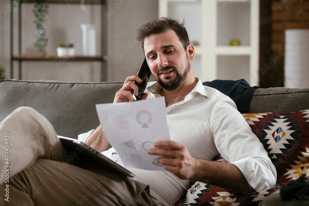 Young man working from home. Businessman at home on sofa with laptop and phone Young man working from home. Businessman at home on sofa with laptop and phone