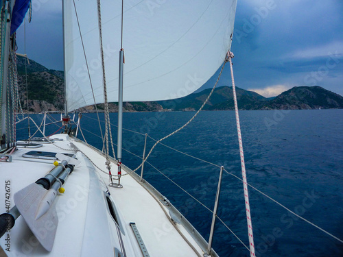 Aboard a sailboat yacht with main sail and genoa on ocean sea with mountain background