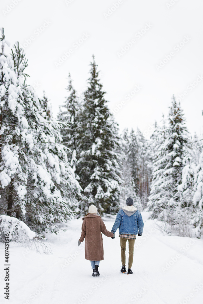 love, happiness and relationship concept - back view of couple walking in winter forest