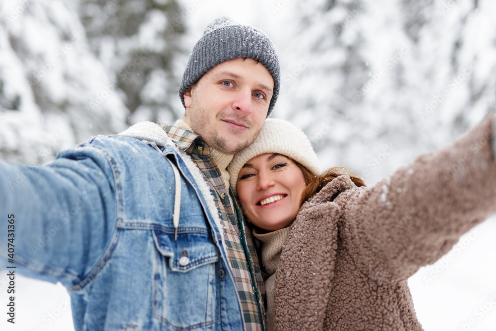 happy couple hugging and taking selfie photo in winter forest