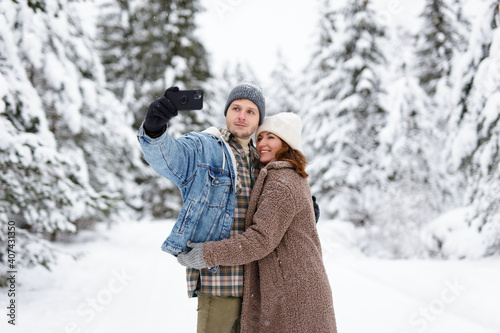 happy beautiful couple hugging and taking selfie photo with smart phone in winter forest