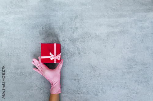 Love gift. Valentine day greeting. Covid-19 protection. Hand in medicine glove holding red present box