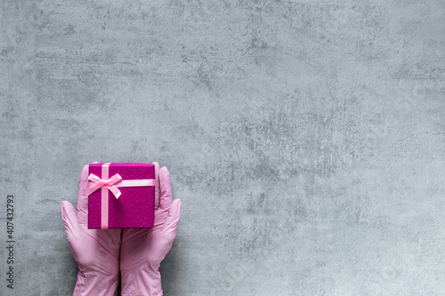 Hands in medicine glove holding pink present box on grey copy space. Advertising background. © Hanna