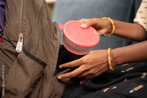 Close up shot of mother hands placing tiffin and water bottle box inside kids schools bag - concept of mother making kid ready for school. photo