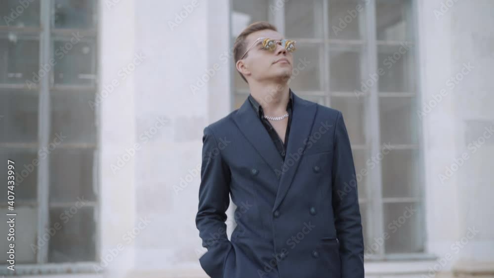 Portrait of stylish wealthy young man in elegant suit putting on sunglasses outdoors. Confident handsome Caucasian businessman standing in city. Lifestyle concept. Portrait of stylish wealthy young man in elegant suit putting on sunglasses outdoors. Confident handsome Caucasian businessman standing in city. Lifestyle concept.