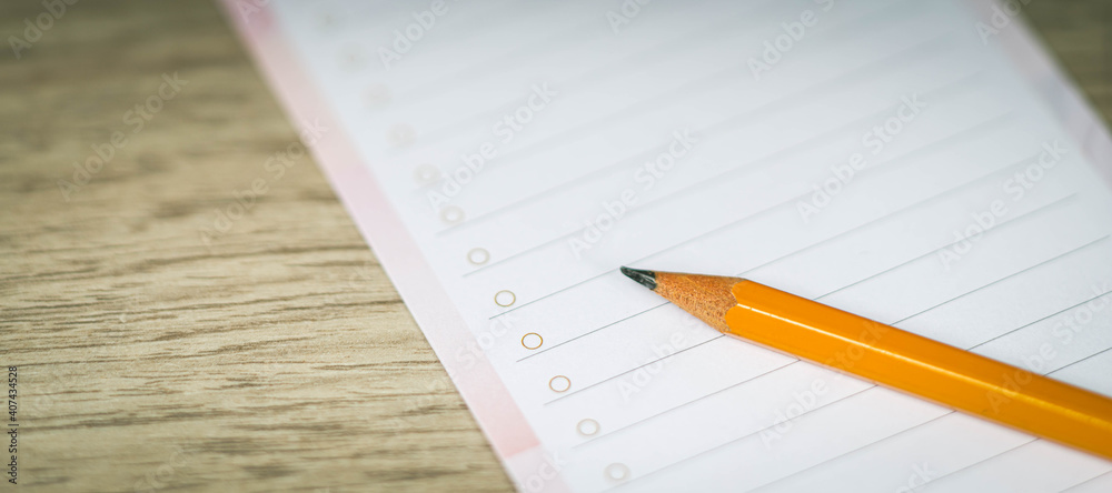 Close-up of pencil on clean white lined paper blank. Wooden table background. Top view. Close-up of pencil on clean white lined paper blank. Wooden table background. Top view.