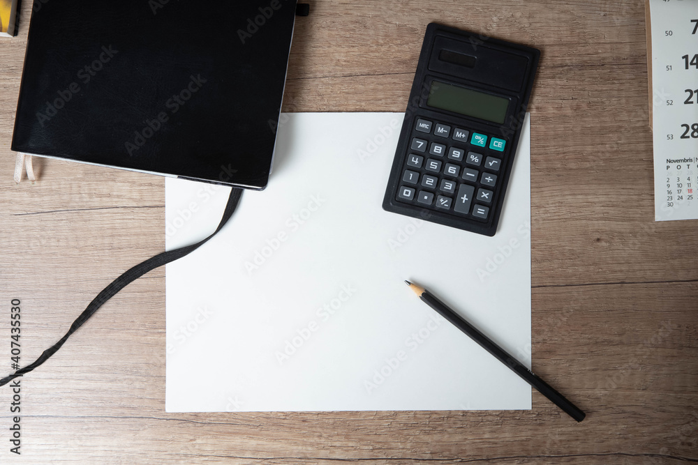 Personal leather bounded journal. Black pencil on empty paper blank. Calculator and calendar on wooden table. Top view. Personal leather bounded journal. Black pencil on empty paper blank. Calculator and calendar on wooden table. Top view.