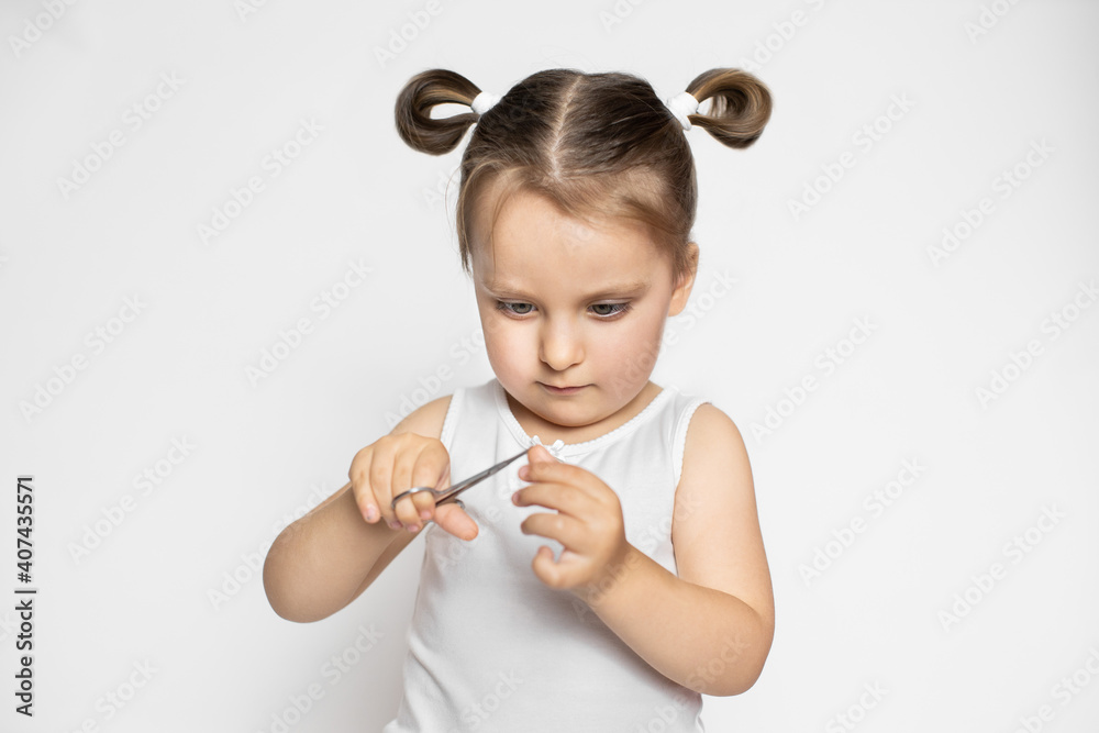 Close up portrait of little cute concentrated 3 years old kid girl, wearing white top and having ponytails hair style, cutting trimming her finger nails. Isolated on white Close up portrait of little cute concentrated 3 years old kid girl, wearing white top and having ponytails hair style, cutting trimming her finger nails. Isolated on white