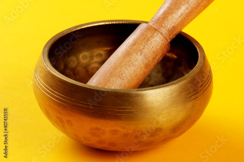 A Tibetan Singing Bowl with a wooden stick on a yellow background, green cloth