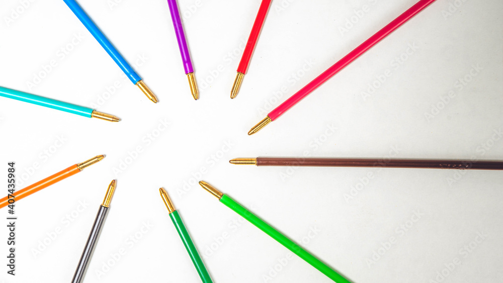 Group of different colors pivots of pens lie on empty white paper blank. Wooden table background. Top view. Group of different colors pivots of pens lie on empty white paper blank. Wooden table background. Top view.