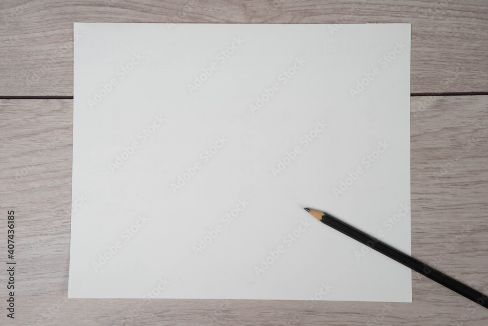 Close-up of pencil on clean white paper blank. Wooden table background. Top view.