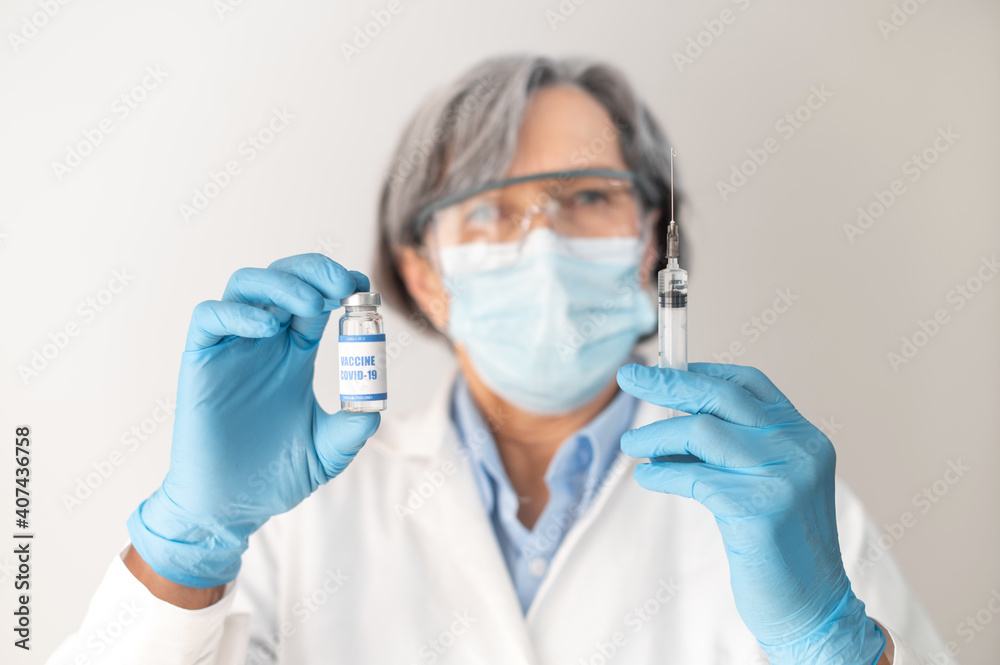Demonstration of a coronavirus vaccine, close-up of a researcher doctor healthcare professional in goggles, face mask and latex gloves holding a covid-19 vaccine and syringe ready for clinical trial Demonstration of a coronavirus vaccine, close-up of a researcher doctor healthcare professional in goggles, face mask and latex gloves holding a covid-19 vaccine and syringe ready for clinical trial