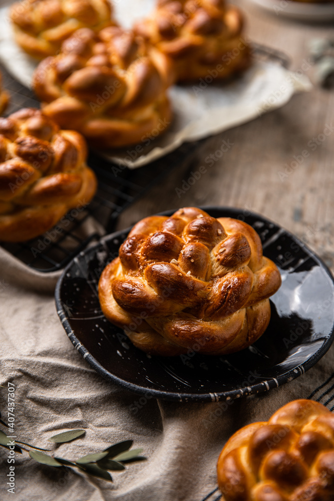 Homemade brioche knot buns on black plate and cooling rack on wooden table. Homemade brioche knot buns on black plate and cooling rack on wooden table.