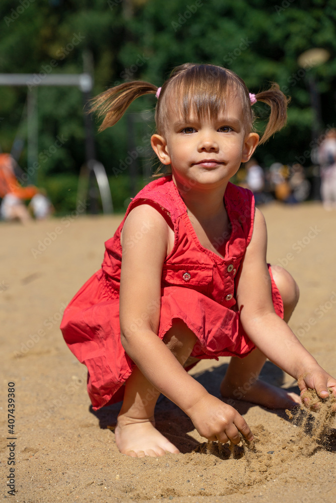 little girl in a red dress plays with sand on the beach. look at the ...