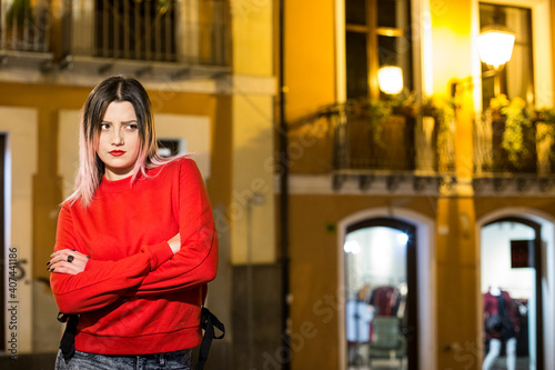 Bella ragazza bionda con maglione rosso incrocia le braccia con aria severa, in contesto urbano