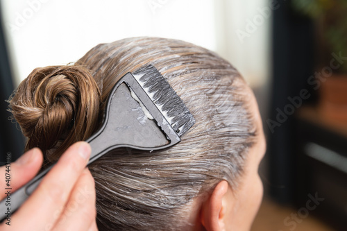 Hairdresser applying bleach or hair color for hair dye with a black brush at home or salon. photo