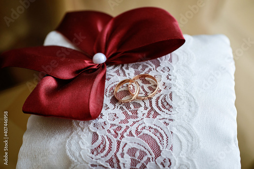 gold wedding rings on a white cushion with red bows and ornaments. close-up, macro