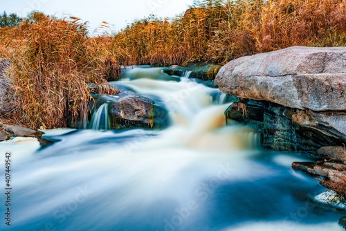 Fototapeta Naklejka Na Ścianę i Meble -  Stream runs among white wet stones covered with grass in golden autumn
