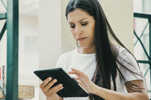 Content deliveryman waiting when woman checking order. Beautiful female client looking for information about her parcel via tablet and standing outdoors. Delivery service and online shopping concept
