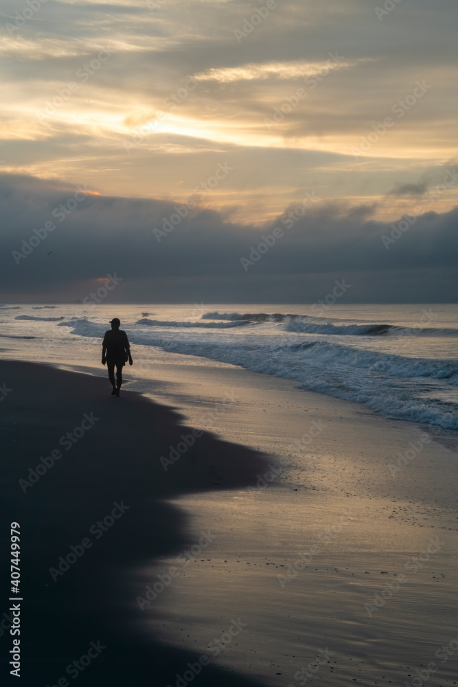 Naklejka premium silhouette of a person walking on the beach at sunrise