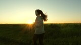 Young woman athlete runner breathing fresh air in morning. Healthy beautiful girl doing fitness jogging on wheat field. Training run. Free woman runs in summer at dawn listens to music with headphones