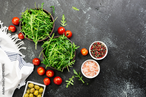 Fresh arugula salad leaves, olives and cherry tomatoes in two clay bowls on black rustic background with copy space for your design. Healthy diet food concept. Restaurant menu, cooking blog template. 