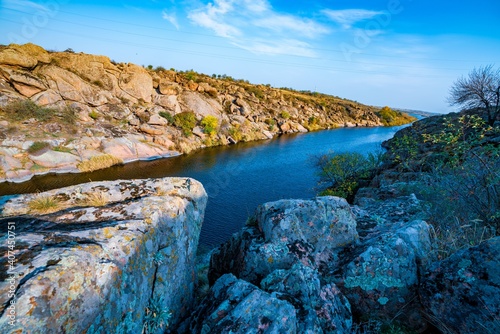 A large number of stone minerals covered with vegetation lying over a small river in picturesque Ukraine