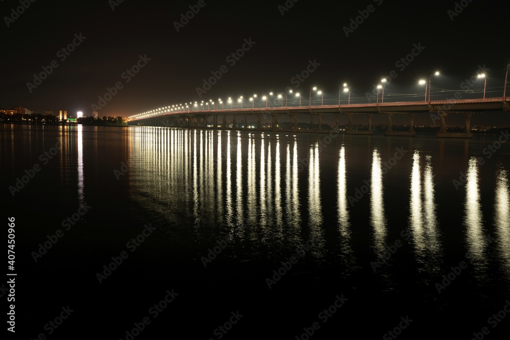 Reflection of bright lanterns in the Dnieper river under the bridge