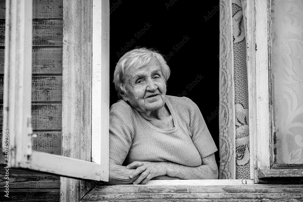 An elderly woman sitting and looking out the window. Black and white photo. An elderly woman sitting and looking out the window. Black and white photo.