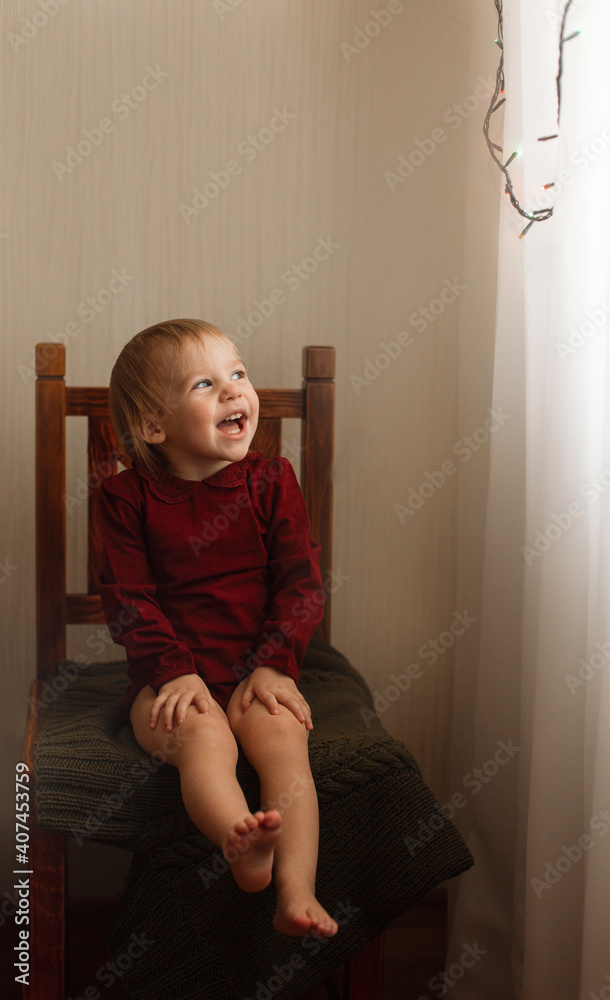 a girl in a burgundy bodysuit sits on a wooden chair, looks out the window and smiles a girl in a burgundy bodysuit sits on a wooden chair, looks out the window and smiles