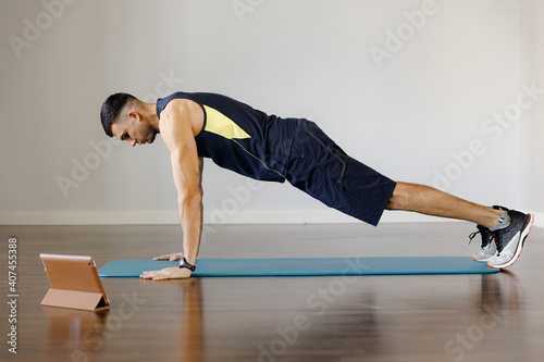 A young handsome man does an exercise in an online workout. The emphasis is standing on your hands for push-ups. Playing sports at home with a tablet