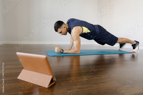 A young sports man does a plank exercise in self-isolation conditions. Online training at home with a social distance. Training all groups of mice by static load