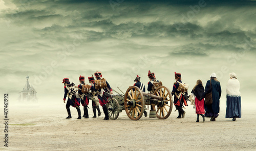 Napoleonic soldiers and women marching and pulling a cannon through plain land, countryside with stormy clouds. Soldiers going towards a russian orthodox church on horizon. No recognizable persons. photo