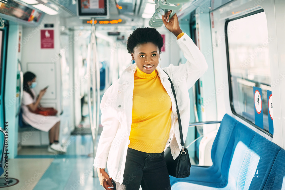 A smiling young African woman holds on to a handrail while standing on a subway train during her daily commute to work A smiling young African woman holds on to a handrail while standing on a subway train during her daily commute to work