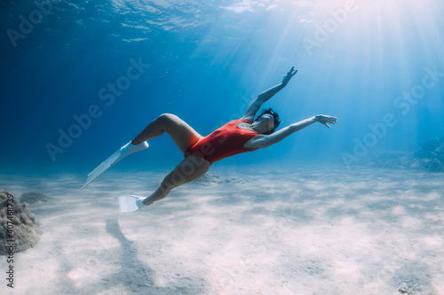 Woman freediver in red swimsuit with white fins posing underwater in tropical ocean. Sporty girl dive underwater.