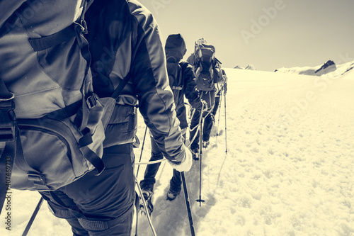 Rope team member point of view with mountaineers walking on snow and ice in sunny weather.