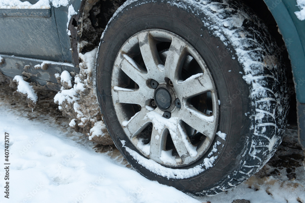 Parts of the car are covered with snow and ice after a snowfall. Wheel close-up in dirt and anti-icing reagents. Big frosts and a lot of snow in the city. Problems on winter slippery roads.