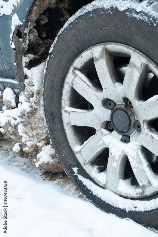 Parts of the car are covered with snow and ice after a snowfall. Wheel close-up in dirt and anti-icing reagents. Big frosts and a lot of snow in the city. Problems on winter slippery roads.