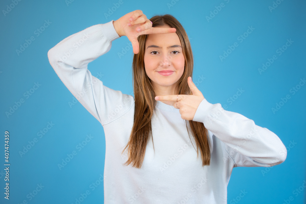 teen girl making photo frame gesture over blue background teen girl making photo frame gesture over blue background