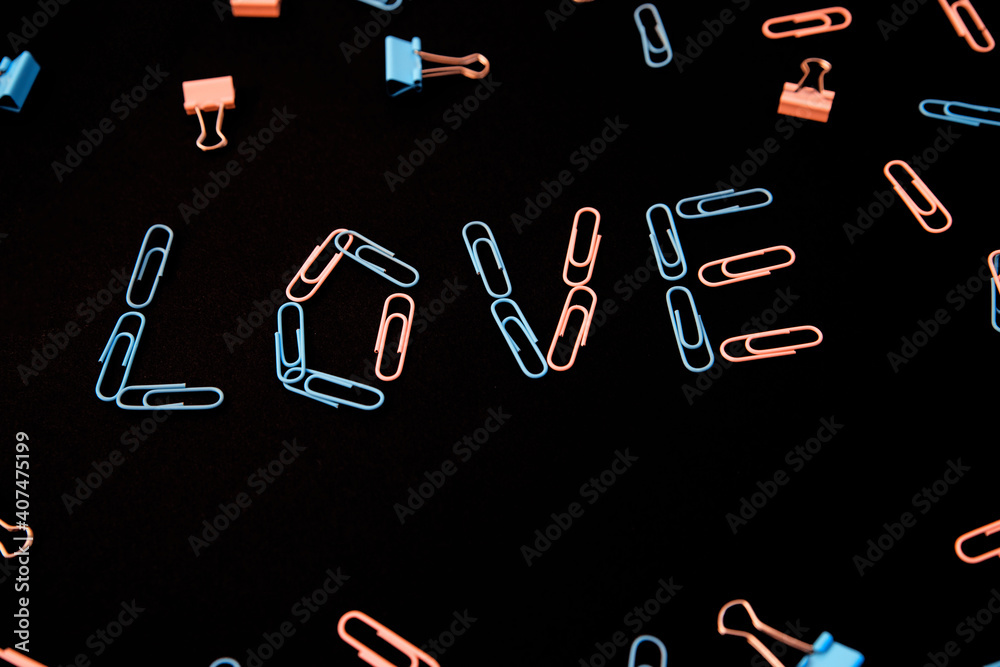 The word love is laid out from paper clips on a black background. The paper clips are pink and blue. The word love is laid out from paper clips on a black background. The paper clips are pink and blue.