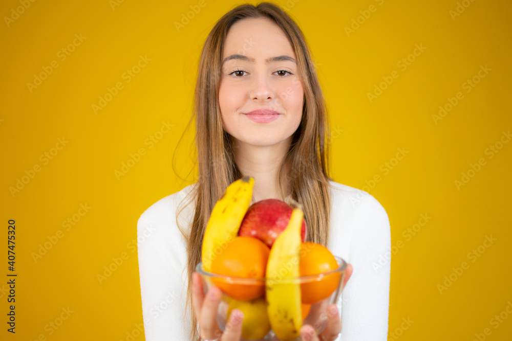 Happy beautiful girl holding bowl of fresh fruits, studio shot, isolated over yellow background Happy beautiful girl holding bowl of fresh fruits, studio shot, isolated over yellow background